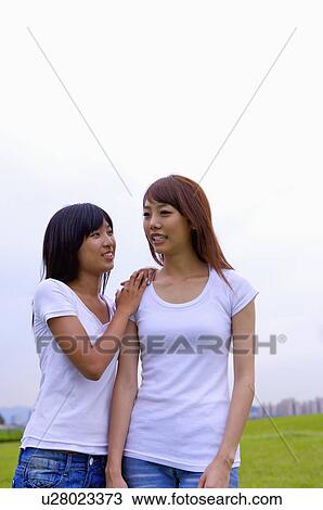 Stock Image - Two girls standing on the lawn together and smiling, Teenager. Fotosearch