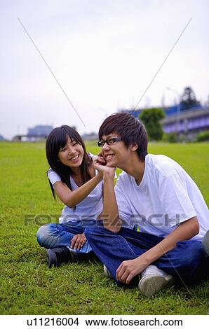 Picture - Young boy and girl sitting on the lawn and smiling happily, Teenager. Fotosearch