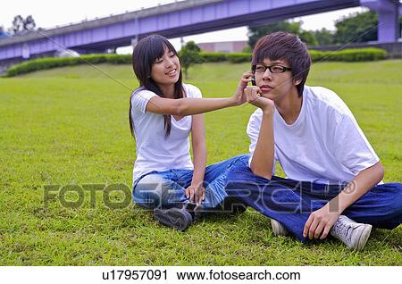 Stock Image - Young girl and boy sitting on the lawn together, Teenager. Fotosearch