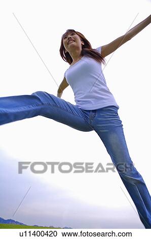 Stock Image - Young girl jumping with arms outstretched, Teenager. Fotosearch