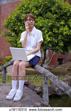 Teenager girl sitting on the baluster, holding mobile phone and using laptop, Teenager View Large Photo Image Stock Photography - Teenager girl sitting on the baluster, holding mobile phone and using laptop, Teenager. Fotosearch