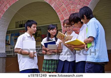 Stock Photo - Teenagers standing in the campus and discussing with book together, Teenager. Fotosearch
