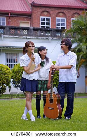 Stock Image - Teenagers standing on the lawn with a guitar and smiling happily, Teenager. Fotosearch