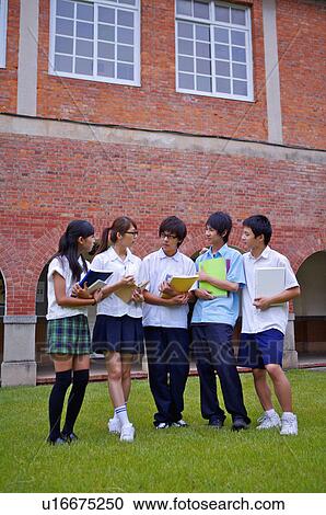 Stock Image - Teenagers standing on the lawn with books and discussing together, Teenager. Fotosearch