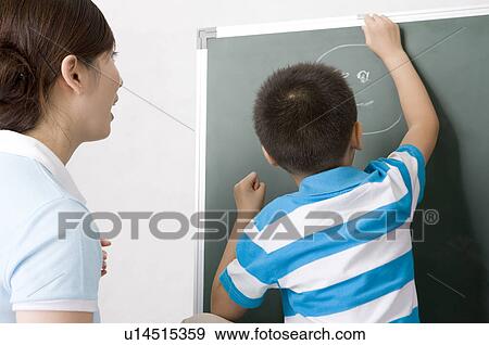 Stock Photo - Little boy drawing on the blackboard with his mother standing behind, Family, Leisure Activities. Fotosearch