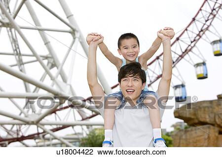 Stock Image - Little boy riding on father's neck with arms outstretched and smiling happily, Family, Leisure Activities. Fotosearch