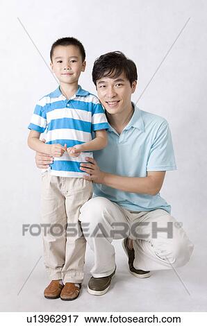 Stock Photo - Man crouching with little boy and looking at the camera together, Family, Leisure Activities. Fotosearch