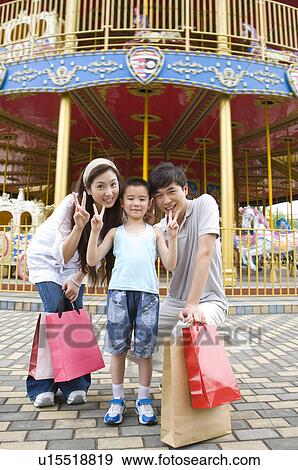 Stock Photo - Young family with little boy standing in the amusement park with shopping bags and gesturing with smile, Family, Leisure Activities. Fotosearch