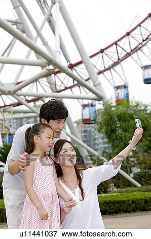 Young family with little girl standing in the amusement park and taking photos, Family, Leisure Activities View Large Photo Image Stock Photo - Young family with little girl standing in the amusement park and taking photos, Family, Leisure Activities. Fotosearch