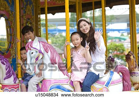 Picture - Young family with two children sitting on the carrousel and smiling happily, Family, Leisure Activities. Fotosearch