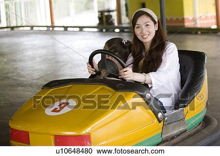 Stock Image - Young woman playing bumper car with little girl and gesturing with smile, Family, Leisure Activities. Fotosearch