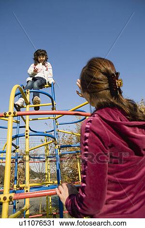 Stock Image - Mother watching daughter on jungle gym. Fotosearch