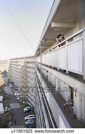 Stock Image - Two women looking down from hallway of housing complex. Fotosearch