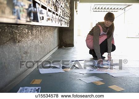 Stock Photo - Woman picking up flyer on porch. Fotosearch