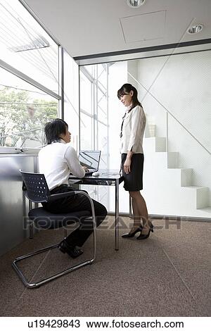 Young man working at his desk with woman standing beside View Large Photo Image Stock Image - Young man working at his desk with woman standing beside. Fotosearch