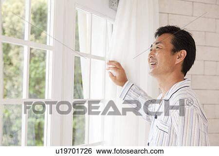 Stock Photograph - Mature man in pajama standing in front of window. Fotosearch