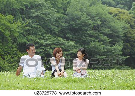 Stock Photo - Three people sitting on grass. Fotosearch