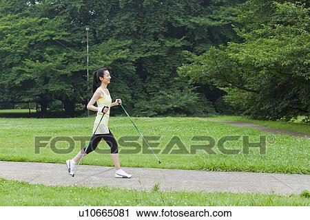 Stock Image - Mid adult woman enjoying Nordic walking. Fotosearch