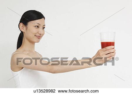 Stock Image - Mid adult woman holding glass of vegetable juice. Fotosearch