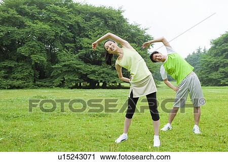 Stock Image - Young man and mid adult woman stretching. Fotosearch