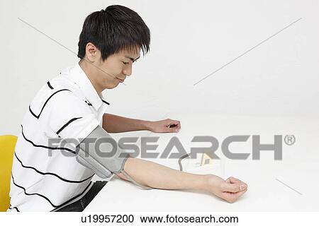 Stock Image - Young man checking blood pressure. Fotosearch