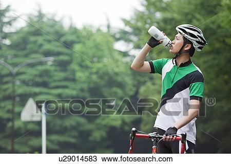 Stock Image - Young man holding bicycle and drinking. Fotosearch