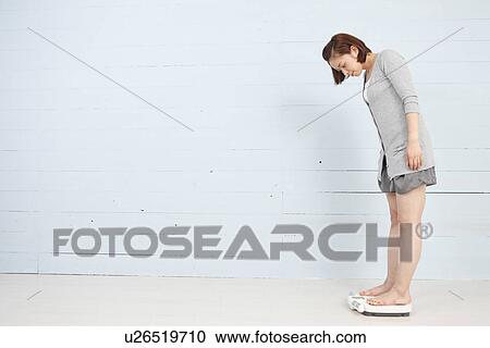 Young woman standing on weight scale View Large Photo Image Stock Image - Young woman standing on weight scale. Fotosearch