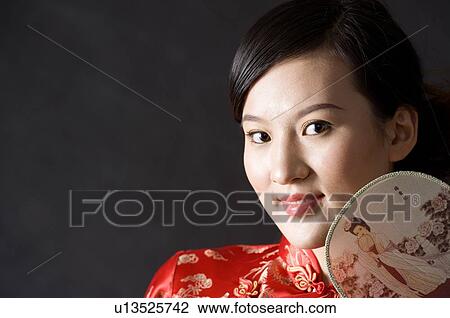 Stock Image - Close-up of young woman in Cheongsam with fan by face posing. Fotosearch