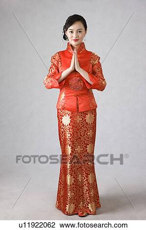 Stock Image - Young woman in cheongsam, hands on chest. Fotosearch