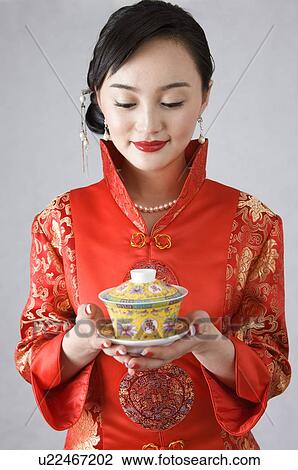 Stock Image - Young woman in cheongsam holding a cup of tea. Fotosearch