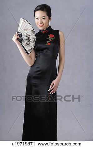 Stock Image - Young woman in cheongsam holding fan. Fotosearch