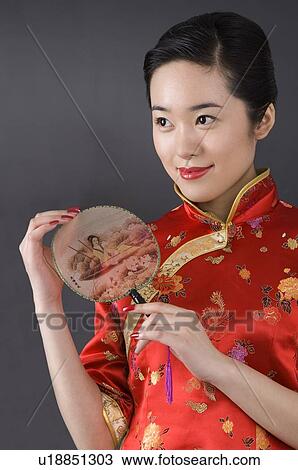 Stock Image - Young woman in cheongsam holding the fan. Fotosearch