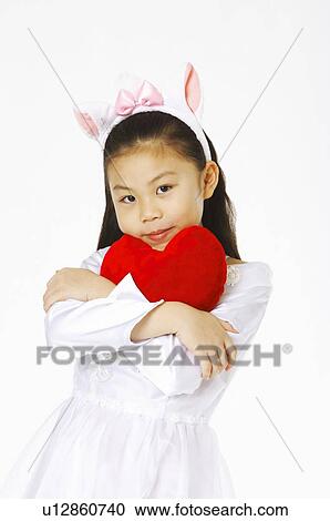 Stock Image - Girl in white skirt holding a red heart in her arms. Fotosearch