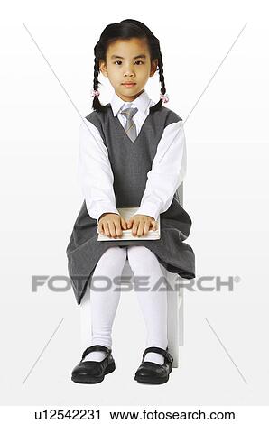 Stock Image - Girl sitting on the chair putting a book on her legs. Fotosearch