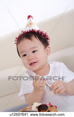 Stock Image - Baby boy wearing party hat holding spoon. Fotosearch