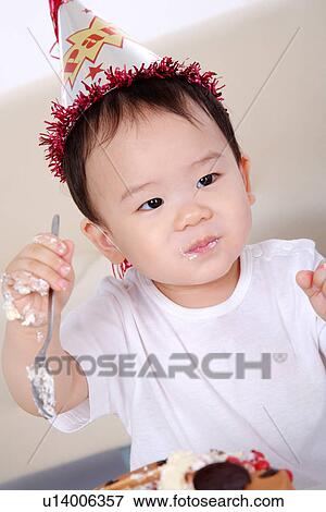Stock Photo - Baby boy wearing party hat holding spoon, smilling, portait. Fotosearch
