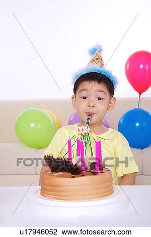 Stock Image - Boy blowing party blower with birthday cake in front of him . Fotosearch