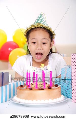 Stock Photo - Girl blowing birthday cake wearing party hat. Fotosearch