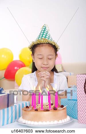 Stock Image - Girl making wish in front of birthday cake. Fotosearch