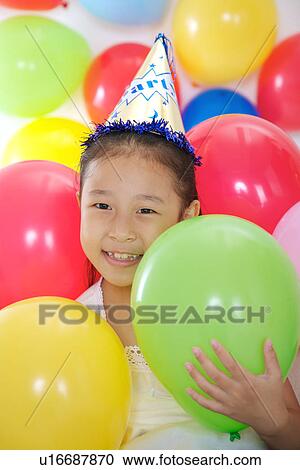 Stock Image - Girl wearing party hat surrounding with balloons. Fotosearch