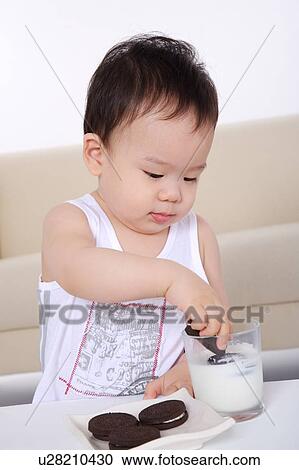 Stock Image - Baby boy dipping a biscuit into a glass of milk. Fotosearch