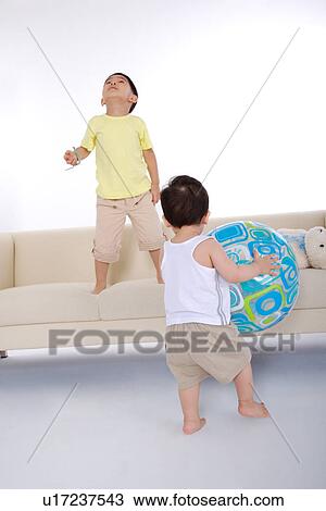 Baby boy holding big ball and boy standing on sofa View Large Photo Image Stock Image - Baby boy holding big ball and boy standing on sofa. Fotosearch