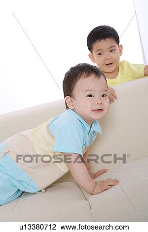 Stock Image - Baby boy on sofa and boy standing by sofa. Fotosearch
