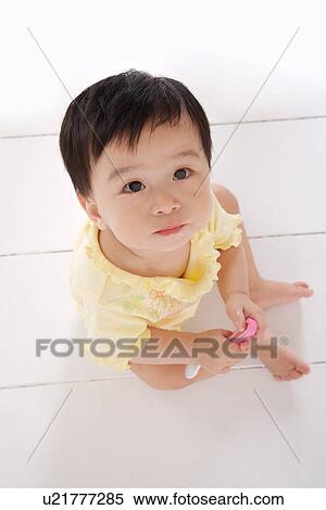 Stock Photography - Baby girl holding spoon sitting on floor looking up, portrait. Fotosearch