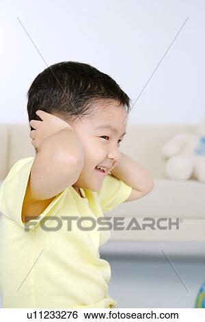 Stock Photograph - Boy covering his ears, smiling, portrait. Fotosearch