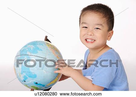 Stock Image - Boy touching globe looking at camera, smiling, portrait. Fotosearch