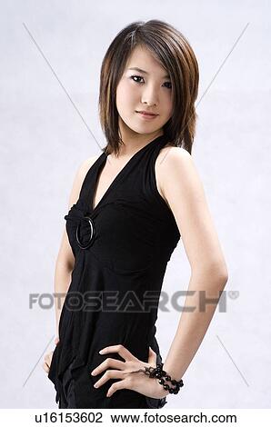 Stock Image - Smiling young woman in a black dress, side view, arms akimbo. Fotosearch