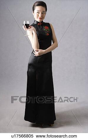 Smiling young woman wearing a black cheongsam with embroidery, holding a glass of wine View Large Photo Image Stock Photography - Smiling young woman wearing a black cheongsam with embroidery, holding a glass of wine. Fotosearch