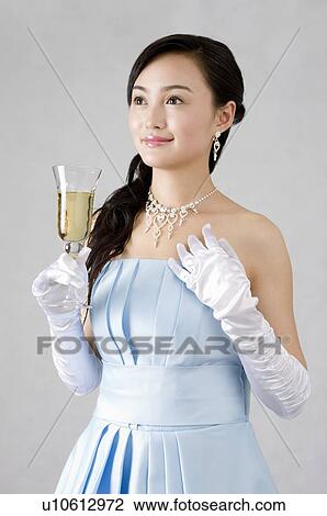 Smiling young woman wearing a blue evening gown, dressed up, holding a glass of champagne View Large Photo Image Stock Image - Smiling young woman wearing a blue evening gown, dressed up, holding a glass of champagne. Fotosearch
