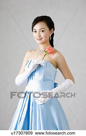 Stock Photo - Smiling young woman wearing a blue dress, holding a pink rose. Fotosearch